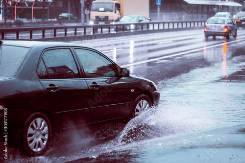Ukraine. Kiev - 05,12,2019 Spraying water from the wheels of a vehicle moving on a wet city asphalt road. The wet wheel of a car moves at a speed along a puddle on a flooded city road during rain.