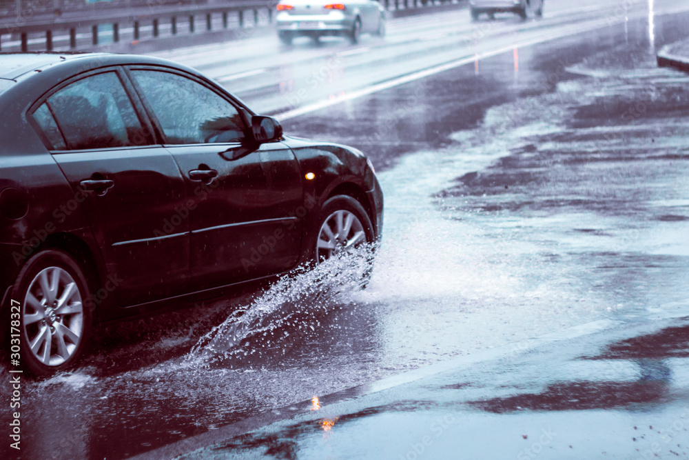 Ukraine. Kiev - 05,12,2019 Spraying water from the wheels of a vehicle moving on a wet city asphalt road. The wet wheel of a car moves at a speed along a puddle on a flooded city road during rain. Ukraine. Kiev - 05,12,2019 Spraying water from the wheels of a vehicle moving on a wet city asphalt road. The wet wheel of a car moves at a speed along a puddle on a flooded city road during rain.