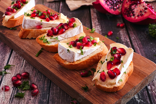Holiday crostini appetizers with brie cheese, pomegranates and parsley. Close up on a serving board against a rustic wood background. Party food concept. photo