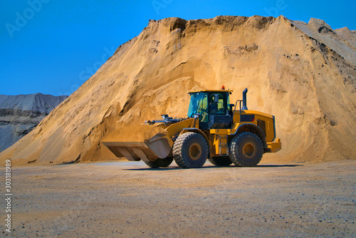 Maintenance of yellow excavator on a construction site against blue sky. wheel loader in sandheap background. Selective focus. photo