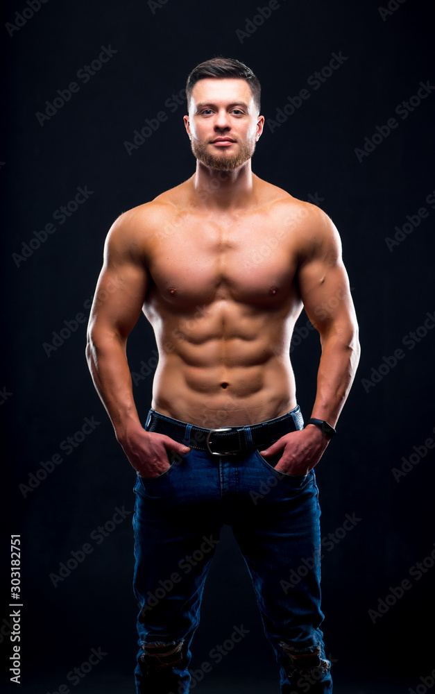 Muscular guy with naked torso posing with hands in pockets. studio photo. Portrait of a handsome man in jeans.