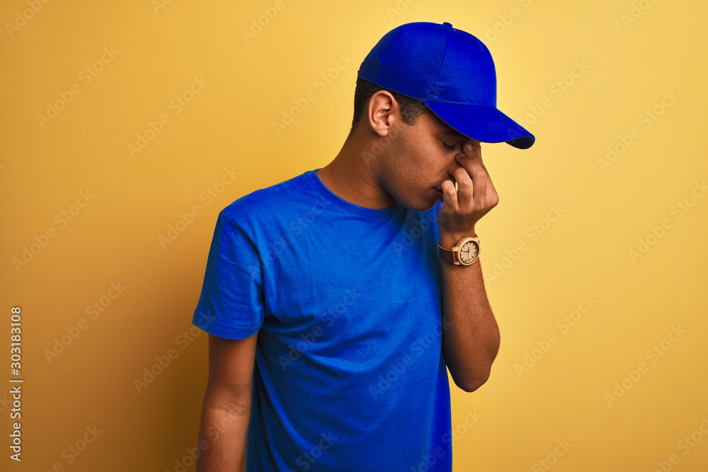 Young handsome arab delivery man standing over isolated yellow background tired rubbing nose and eyes feeling fatigue and headache. Stress and frustration concept.