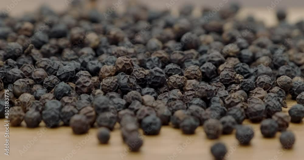 Dolly shot of pile black peppers spread on chopper board with wooden spoon
