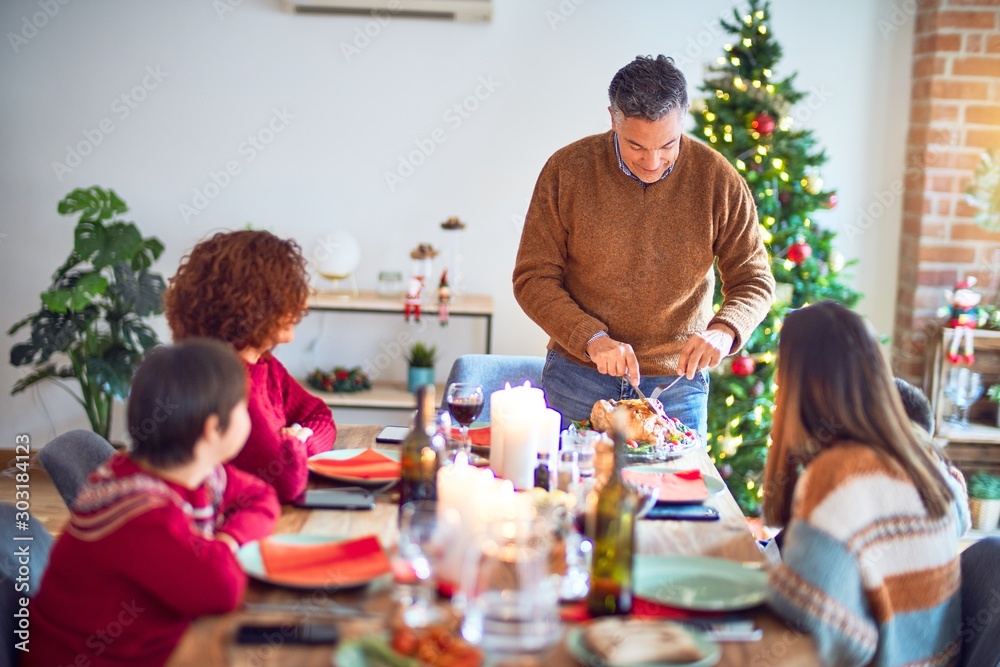 Beautiful family smiling happy and confident. One of them curving roasted turkey celebrating christmas at home Beautiful family smiling happy and confident. One of them curving roasted turkey celebrating christmas at home