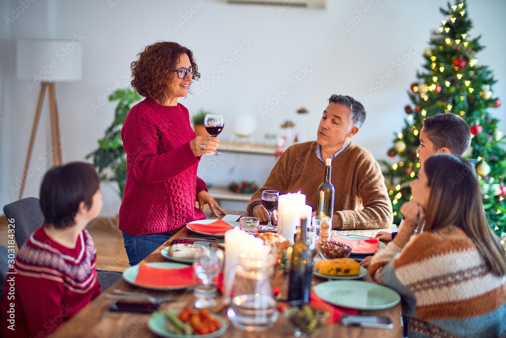 Beautiful family smiling happy and confident. One of them standing holding cup of wine speaking speech celebrating christmas at home Beautiful family smiling happy and confident. One of them standing holding cup of wine speaking speech celebrating christmas at home