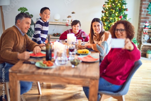 Beautiful family smiling happy and confident. Eating roasted turkey make selfie by smartphone celebrating christmas at home