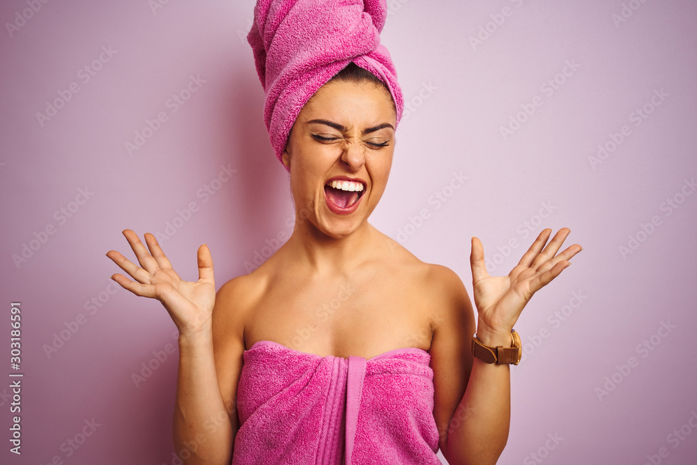 Young beautiful woman wearing towel after shower over isolated pink background celebrating mad and crazy for success with arms raised and closed eyes screaming excited. Winner concept Young beautiful woman wearing towel after shower over isolated pink background celebrating mad and crazy for success with arms raised and closed eyes screaming excited. Winner concept