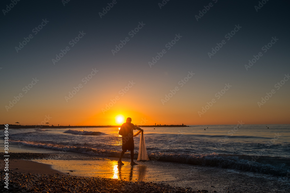 silhouette of fisherman throwing nets at sunrise on a beach of the Valencian community