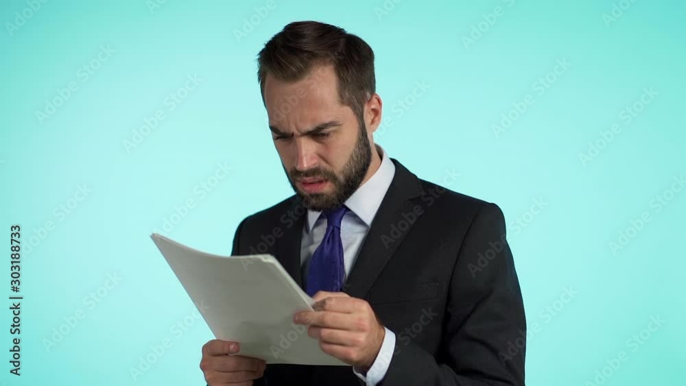 Serious businessman boss isolated on blue background studio.. Man is unsatisfied with work of staff. Young mature male office employee in suit jacket checking documents, reports Serious businessman boss isolated on blue background studio.. Man is unsatisfied with work of staff. Young mature male office employee in suit jacket checking documents, reports