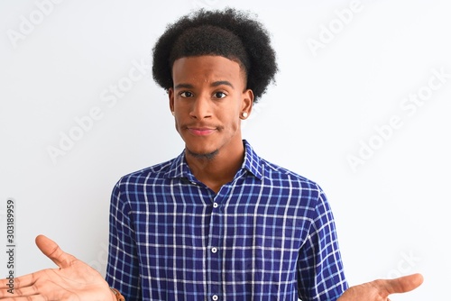 Young african american man wearing casual shirt standing over isolated white background clueless and confused expression with arms and hands raised. Doubt concept.
