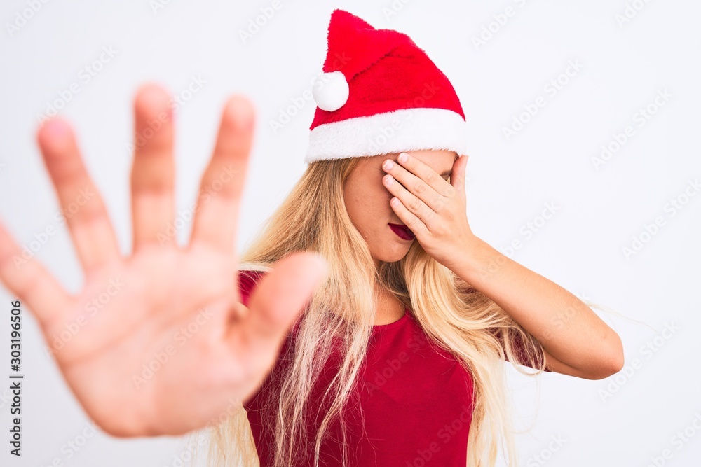 Young beautiful woman wearing Christmas Santa hat over isolated white background covering eyes with hands and doing stop gesture with sad and fear expression. Embarrassed and negative concept.