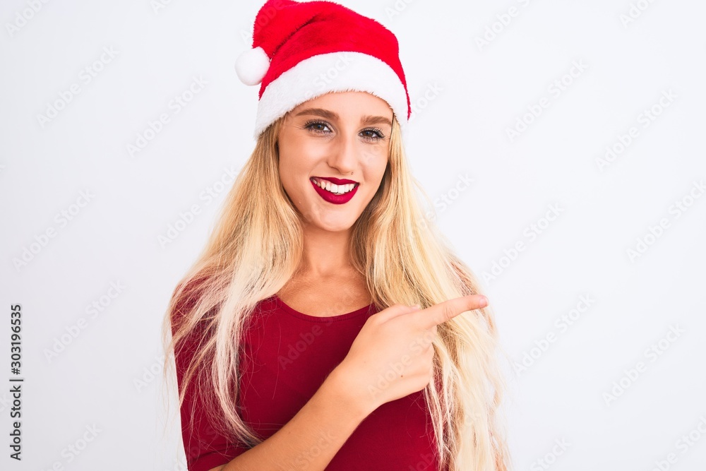 Young beautiful woman wearing Christmas Santa hat over isolated white background cheerful with a smile of face pointing with hand and finger up to the side with happy and natural expression on face Young beautiful woman wearing Christmas Santa hat over isolated white background cheerful with a smile of face pointing with hand and finger up to the side with happy and natural expression on face