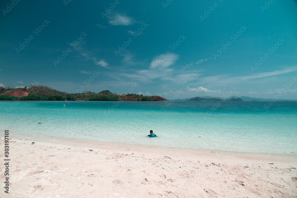 A kid playing in shallow part of a quiet beach in Mahitam Island, Lampung
