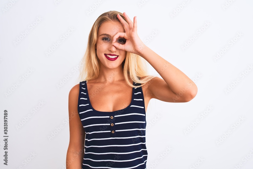 Young beautiful woman wearing casual striped t-shirt standing over isolated white background doing ok gesture with hand smiling, eye looking through fingers with happy face. Young beautiful woman wearing casual striped t-shirt standing over isolated white background doing ok gesture with hand smiling, eye looking through fingers with happy face.
