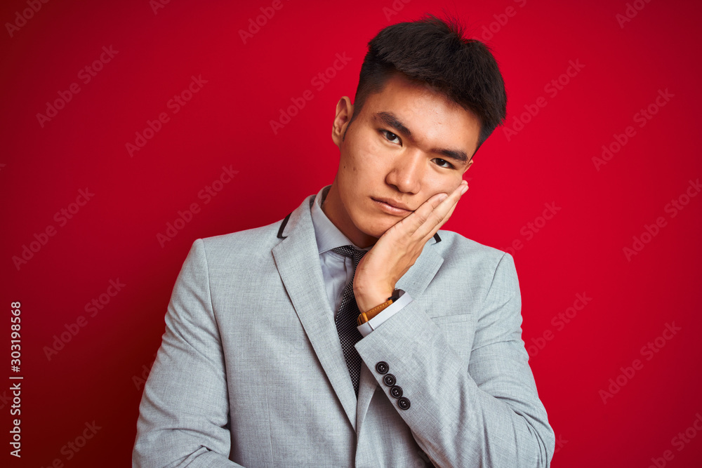 Asian chinese businessman wearing grey jacket and tie standing over isolated red background thinking looking tired and bored with depression problems with crossed arms. Asian chinese businessman wearing grey jacket and tie standing over isolated red background thinking looking tired and bored with depression problems with crossed arms.