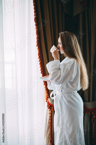 The girl Stit near the window and drinks morning coffee in the hotel room or at home.