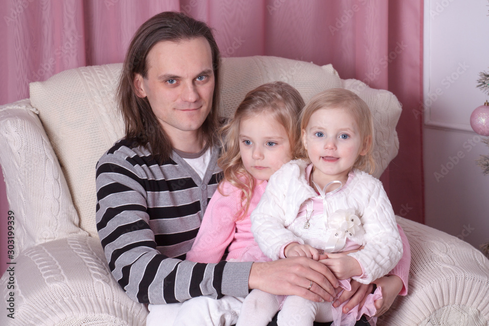 father with two daughters in a chair by the fireplace in the New Year decorations father with two daughters in a chair by the fireplace in the New Year decorations