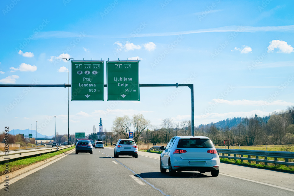 Cars on road with background. Spring cityscape. Town view. Sunny summer day. Adventure travel. Speed line fast motion. Busy street. Outdoor. Holiday. Traffic sign. Highway. Urban landscape in Slovenia