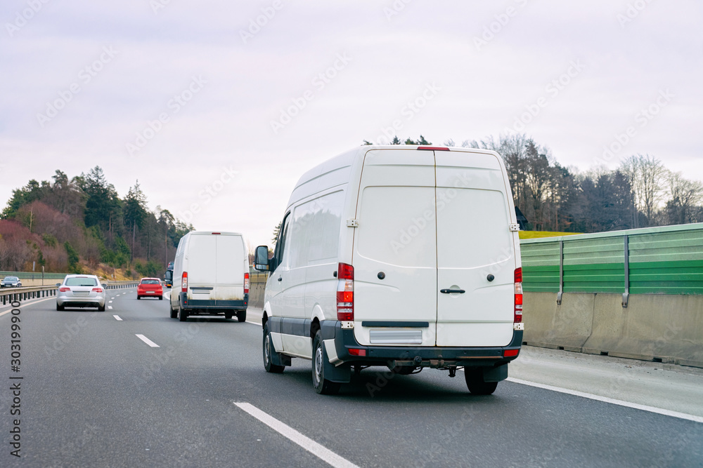 White Minivans in road. Mini van auto vehicle on driveway. European van transport logistics transportation. Auto with driver on highway.