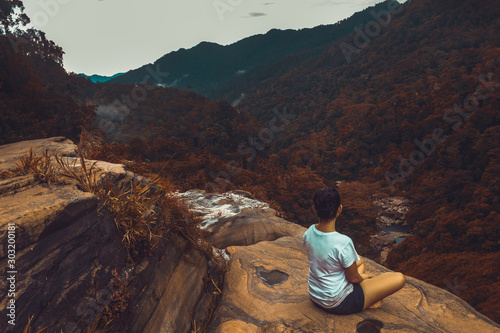 Beautiful Srilankan girl look at distance mountain while sitting on a rock mountain