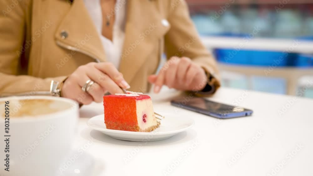 4k video of young woman sitting in cafe, eating deliciouse sweet dessert and browsing photographs in social media using smartphone