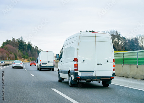 White Minivans on road. Mini van auto vehicle on driveway. European van transport logistics transportation. Auto with driver on highway.