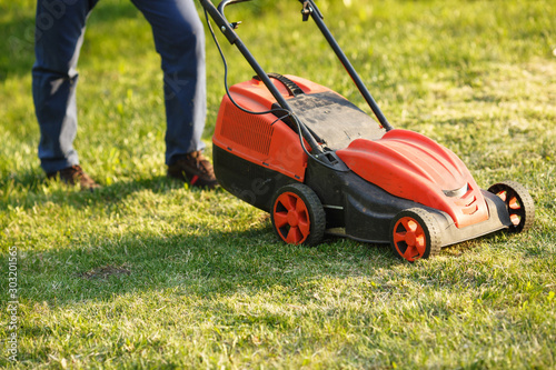 mowing trimmer - worker cutting grass in green yard at sunset. Man with electric lawnmower, lawn mowing. Gardener trimming a garden.