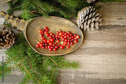 Fresh wild forest red cranberries on a plate with cones and brinch of pine on wooden table flat lay, with copy space photo