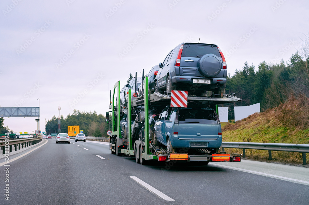 Cars carrier transporter truck in road. Auto vehicles hauler on driveway. European transport logistics at haulage work transportation. Heavy haul trailer with driver on highway.