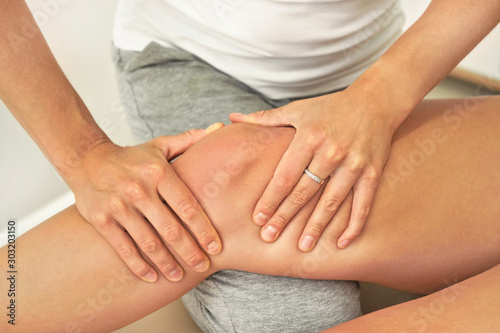 Female caucasian physiotherapist holding massaging knee of patient, closeup on her hands