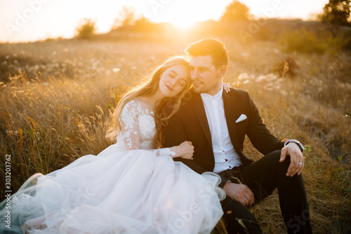 Fototapete Beautoful couple, sitting an huuging in a fied, on marriege day, relaxing on sun