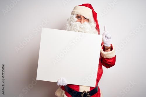 Middle age man wearing Santa Claus costume holding banner over isolated white background surprised with an idea or question pointing finger with happy face, number one © Krakenimages.com