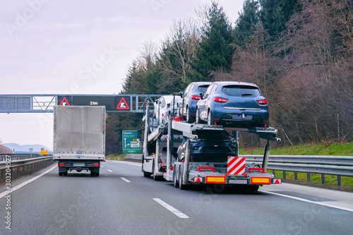 Car carrier transporter truck in road. Auto vehicles hauler on driveway. European transport logistics at haulage work transportation. Heavy haul trailer with driver on highway.