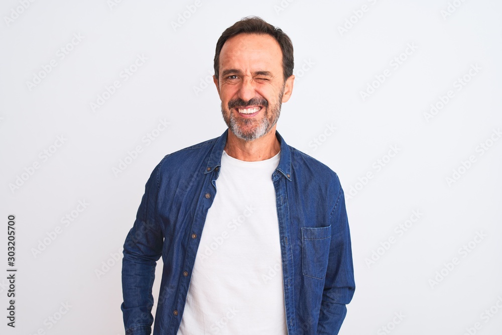 Middle age handsome man wearing blue denim shirt standing over isolated white background winking looking at the camera with sexy expression, cheerful and happy face. Middle age handsome man wearing blue denim shirt standing over isolated white background winking looking at the camera with sexy expression, cheerful and happy face.
