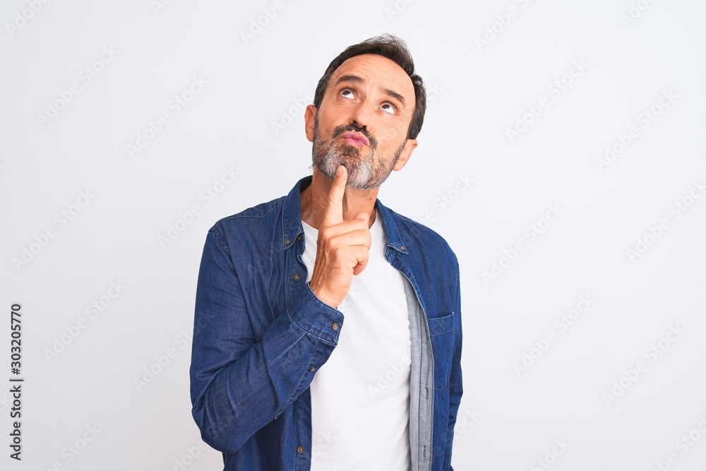 Middle age handsome man wearing blue denim shirt standing over isolated white background Thinking concentrated about doubt with finger on chin and looking up wondering Middle age handsome man wearing blue denim shirt standing over isolated white background Thinking concentrated about doubt with finger on chin and looking up wondering