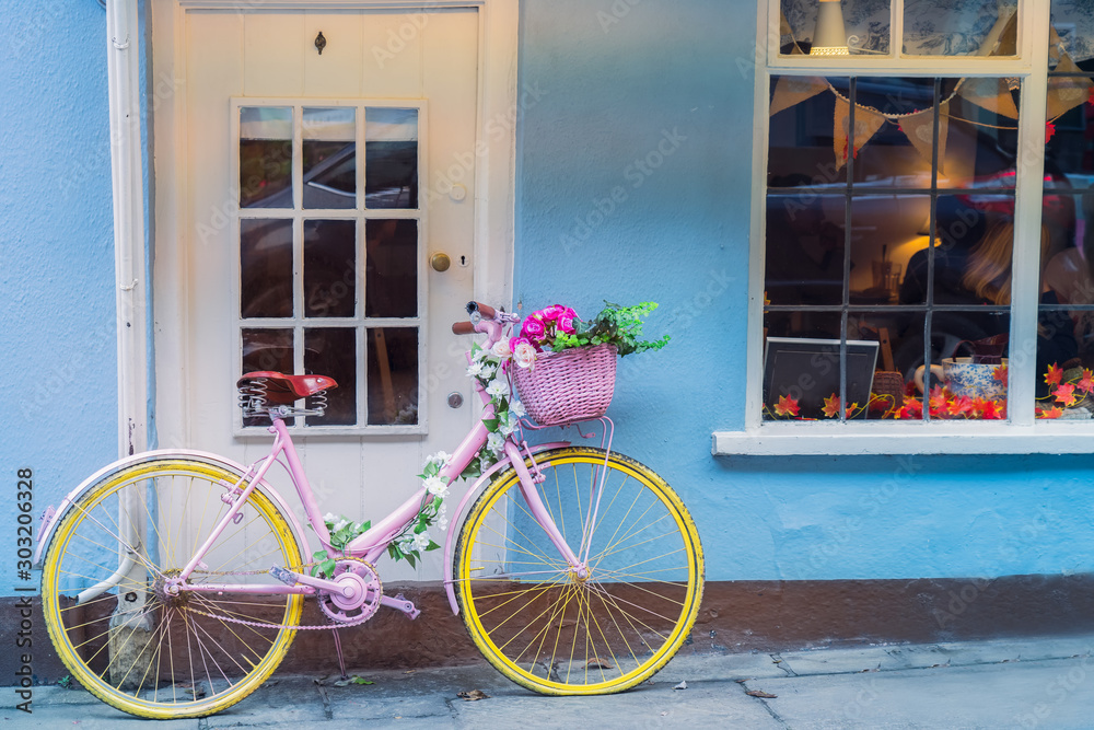 Hipster retro yellow bicycle with flower basket near old english style building with windows and doors with blue walls background. Color if vintage tone. Copy space.