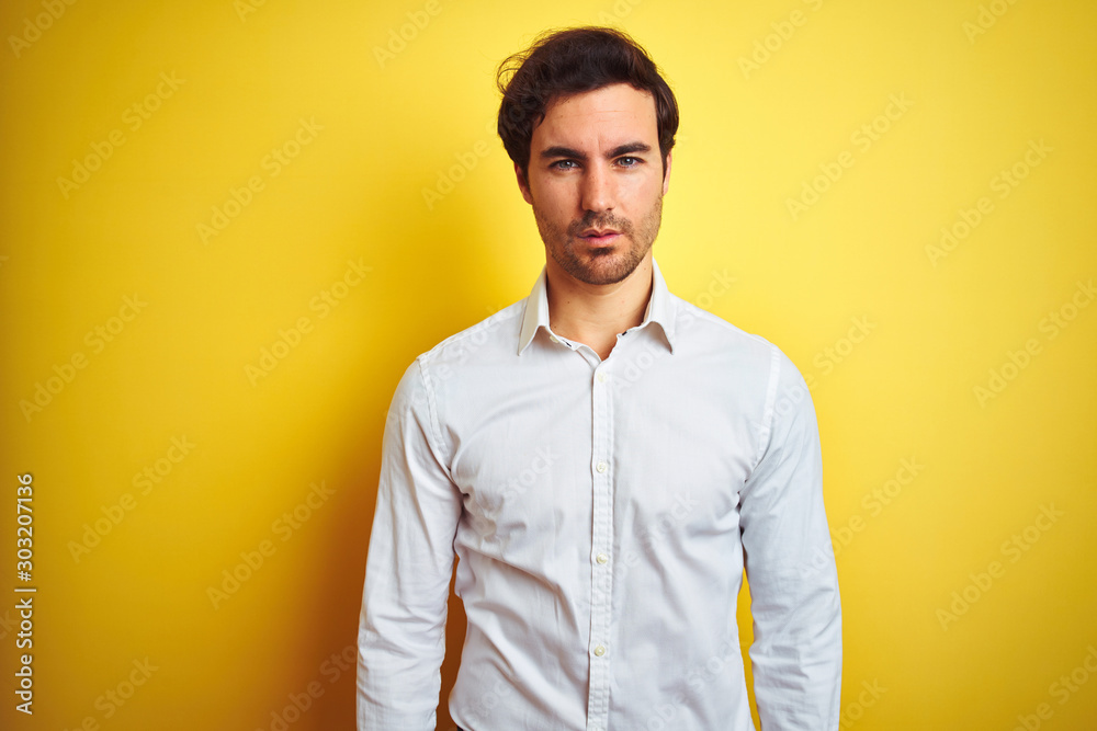 Young handsome businessman wearing elegant shirt standing over isolated yellow background Relaxed with serious expression on face. Simple and natural looking at the camera.