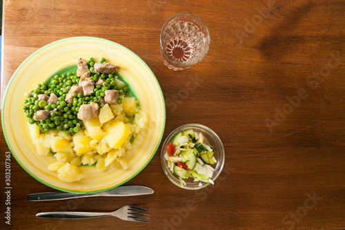 A dinner plate with peas, meat and potatoes with salad and a glass of water