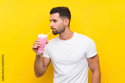 Young man with strawberry milkshake over isolated yellow background