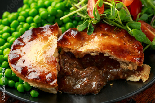 Beef steak pies with rich onion gravy served with sweet peas and salad photo