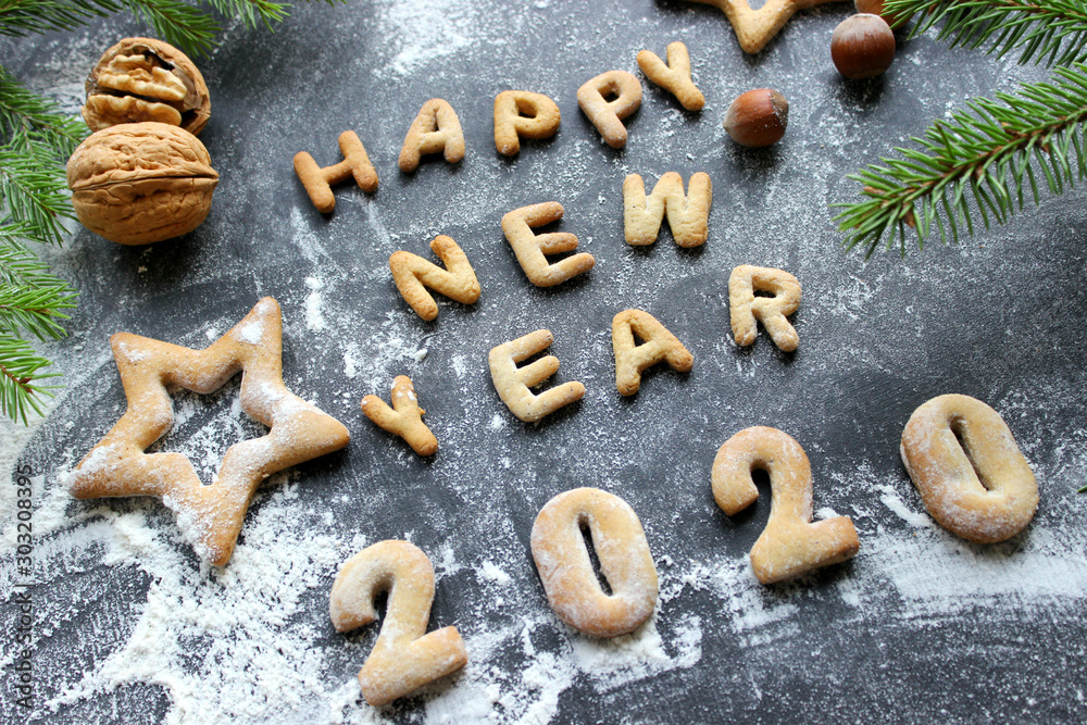 The concept 2020. Baked letters Happy New year and numbers 2020.Greeting card with gingerbread.Christmas card made of gingerbread on a wooden table surrounded by fir branches, nuts, spices and orange. The concept 2020. Baked letters Happy New year and numbers 2020.Greeting card with gingerbread.Christmas card made of gingerbread on a wooden table surrounded by fir branches, nuts, spices and orange.