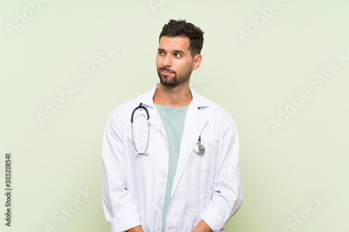 Young doctor man over isolated green wall standing and looking to the side