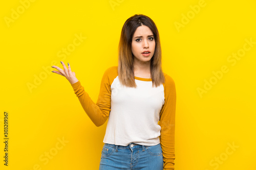 Pretty young woman over isolated yellow wall making doubts gesture