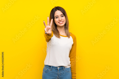 Pretty young woman over isolated yellow wall happy and counting three with fingers