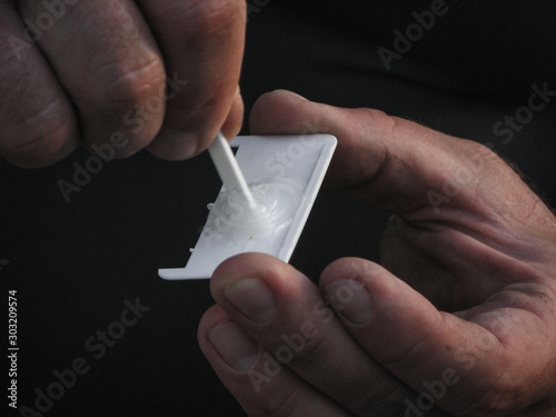 Worker prepairing glue on a small white plastic piece. Man's hands, close up. Glue mixing.