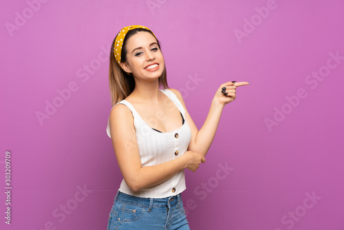Pretty young woman over isolated purple wall pointing finger to the side