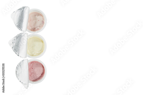 Yogurts of three different flavors in open plastic cups isolated on a white background. Top view. Copy space.