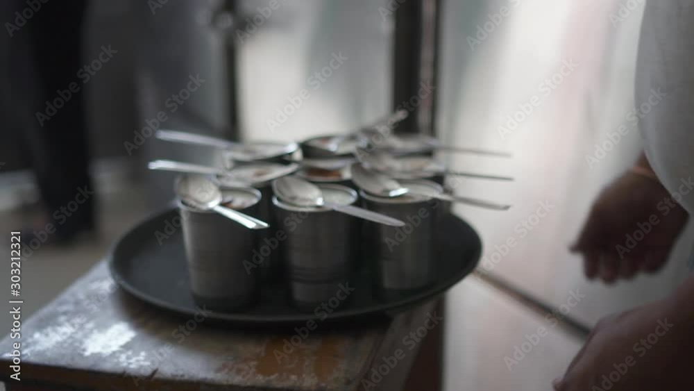 Indian man worker working in local cafe preparing dinner standing in kitchen room. Asian male employee putting spoon on cups with traditional dessert, taking tray in hand. Concept: travel, ethnic Indian man worker working in local cafe preparing dinner standing in kitchen room. Asian male employee putting spoon on cups with traditional dessert, taking tray in hand. Concept: travel, ethnic