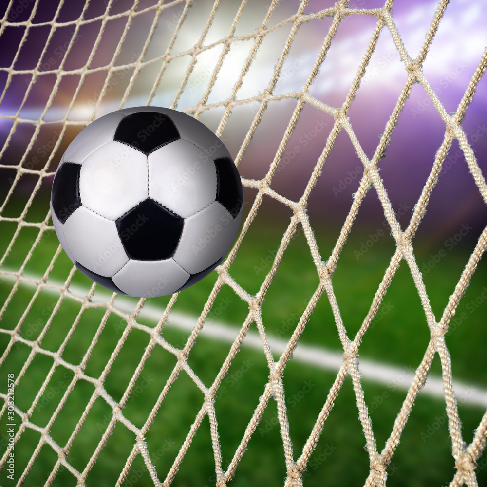 Fototapeta premium A ball in the goal net with a green field and lights on a background