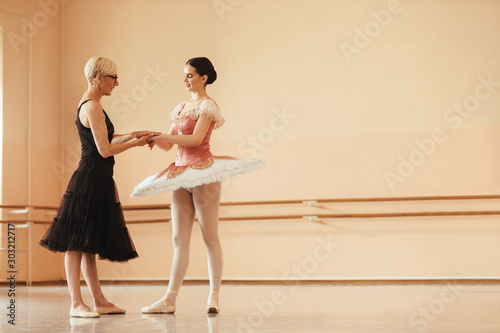 Mature ballet teacher holding hands with a ballerina while talking at dance studio.